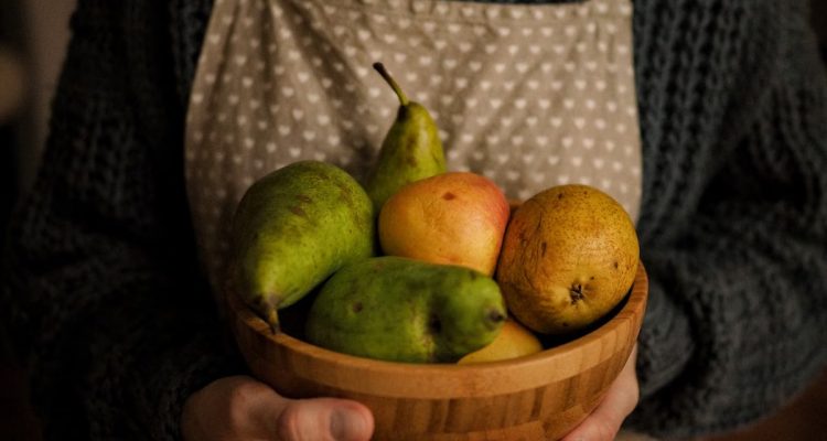 Close-up of a person holding a wooden bowl with fresh fruits including pears.