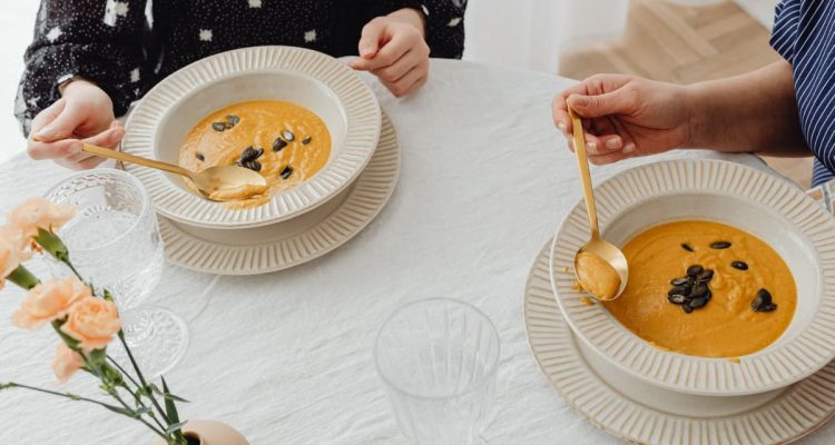 A top view of two people enjoying creamy pumpkin soup with elegant table setting.